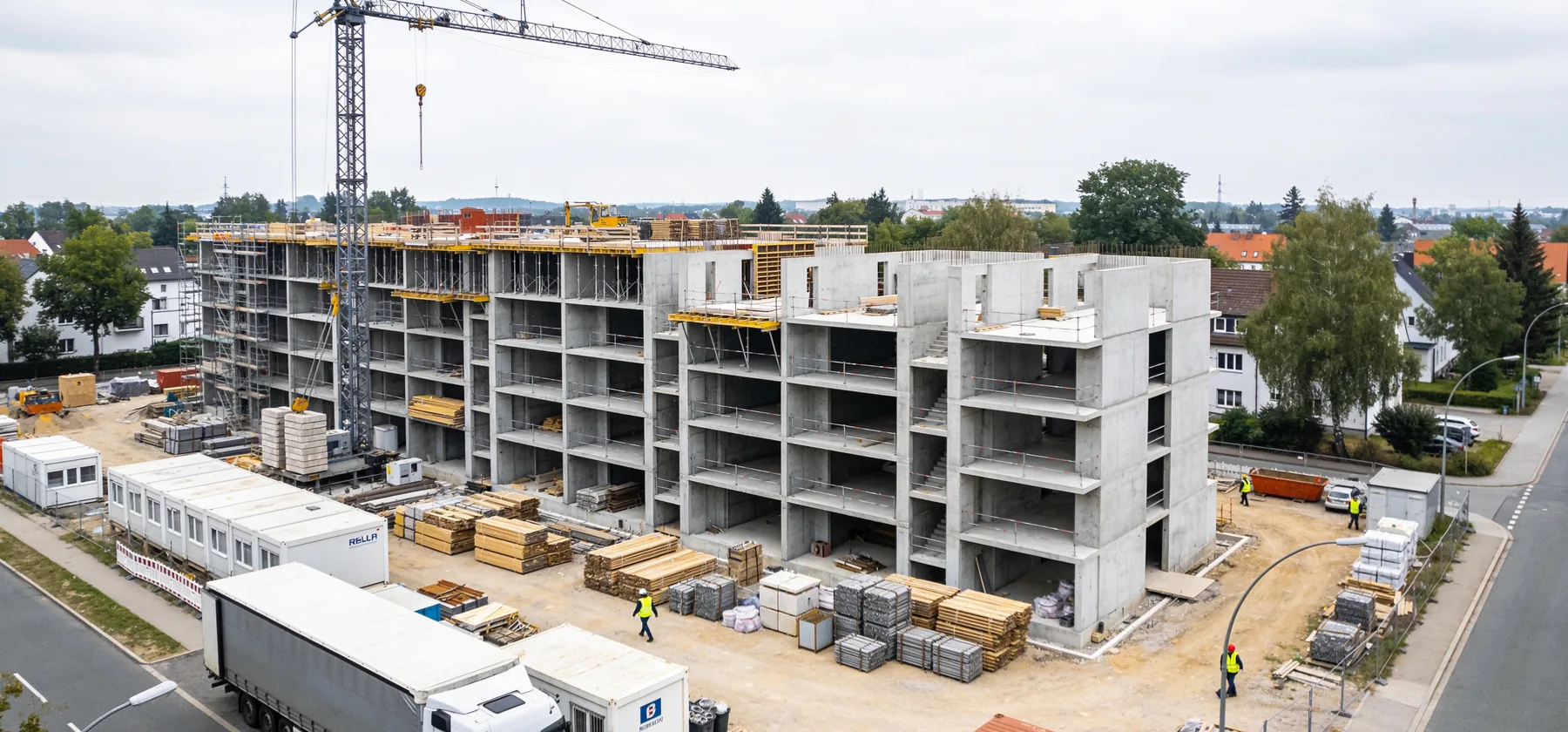 Luftaufnahme einer aktiven Baustelle mit Kran, Rohbau und Materiallager